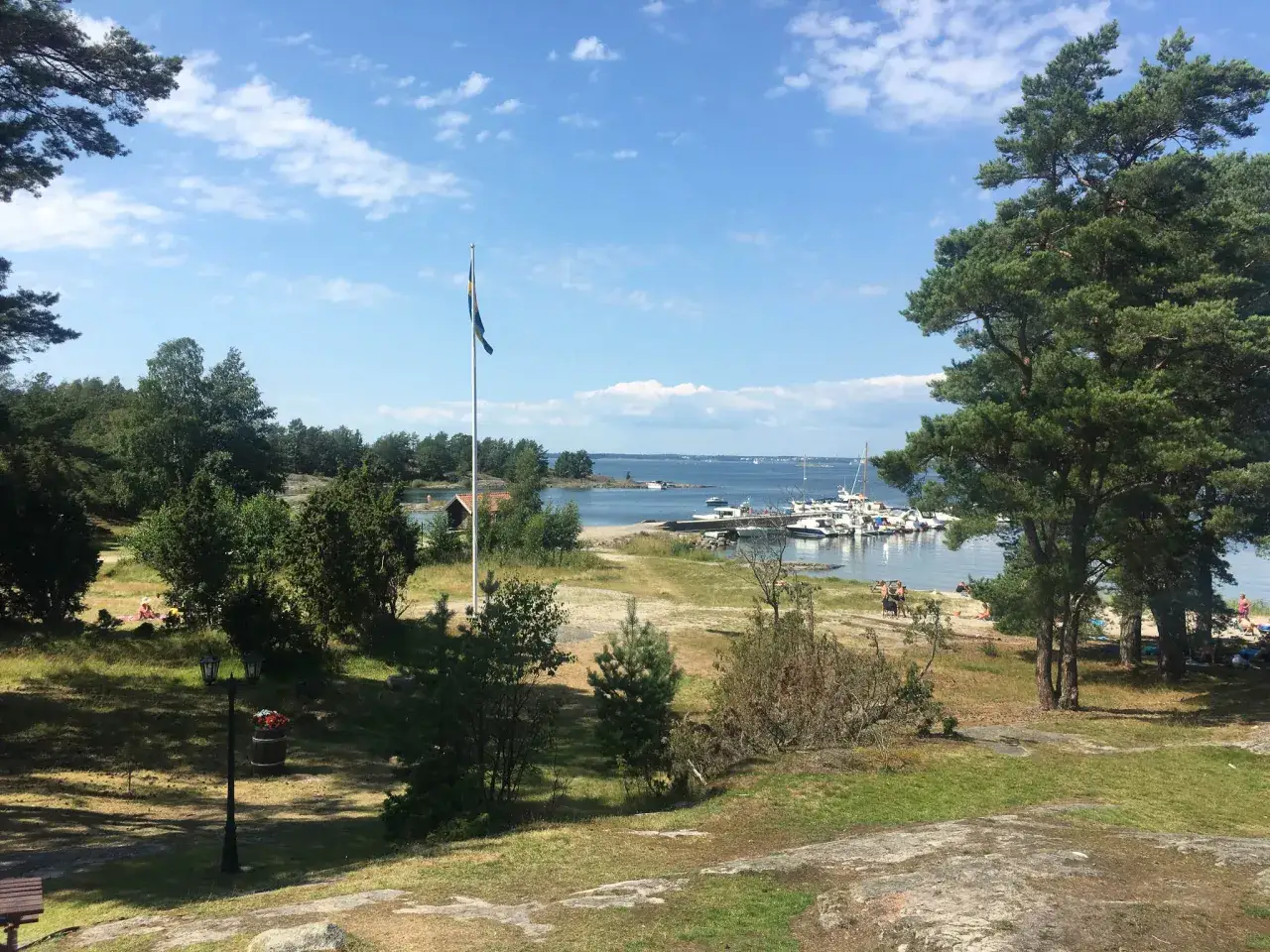 En vacker sommardag f&ouml;r en utflykt i Stockholm. Solen skiner &ouml;ver en hamn med b&aring;tar och m&auml;nniskor som njuter p&aring; stranden.