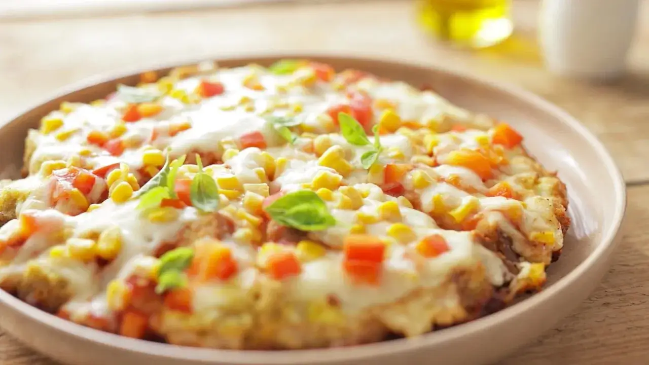 Pyszna pizza z patelni bez drożdży, z kukurydzą, papryką i ciągnącym serem, ozdobiona listkami bazylii.