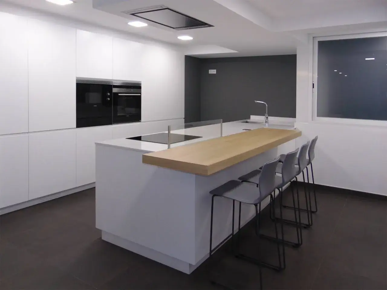 Cocinas modernas con barra de madera, encimera blanca y taburetes grises. Perfectas para disfrutar de un café.