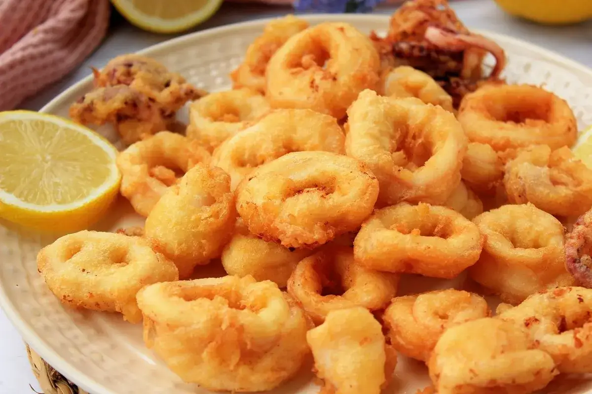Un plato generoso de calamares a la romana dorados y crujientes, acompañados de gajos de limón fresco.
