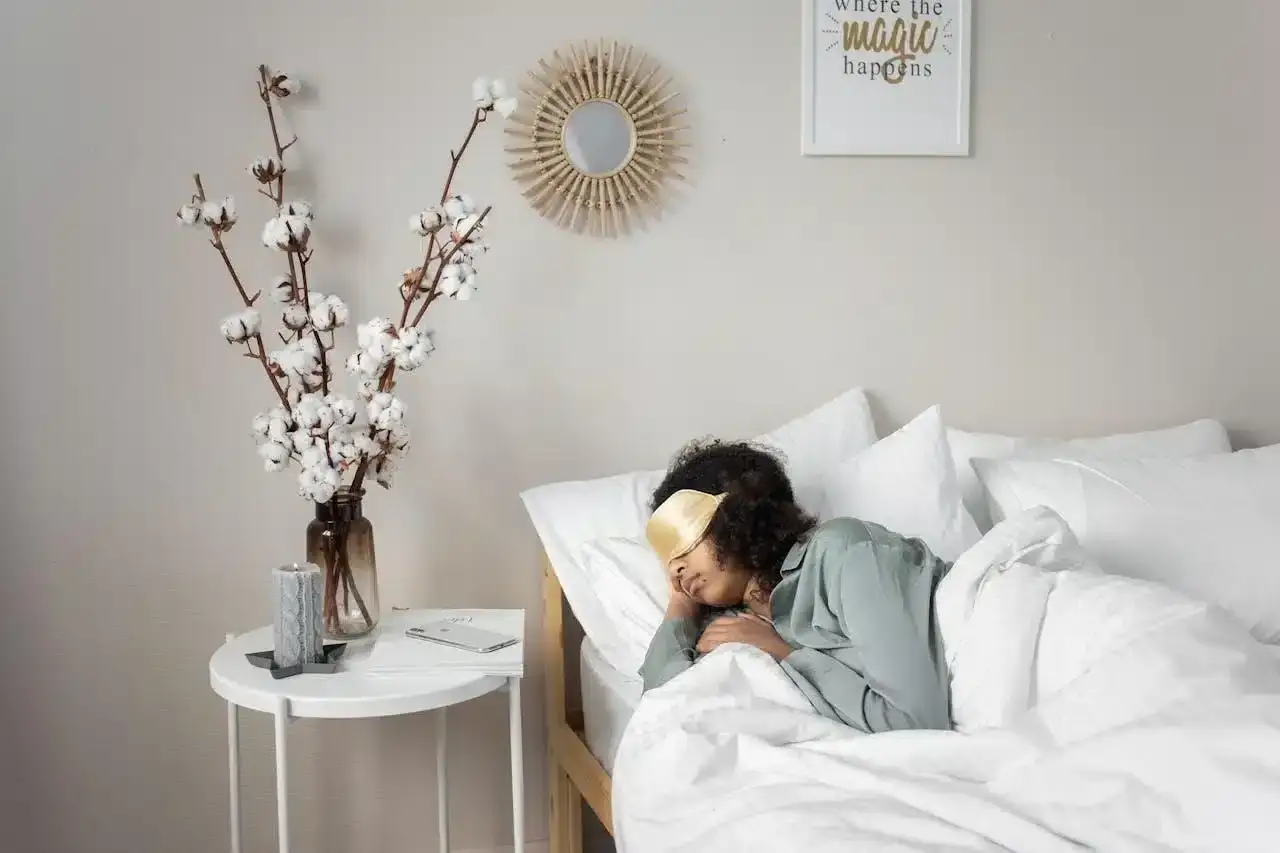 A woman sleeps with an eye mask, hoping to overcome insomnia after surgery. A bedside table holds cotton branches and a candle.