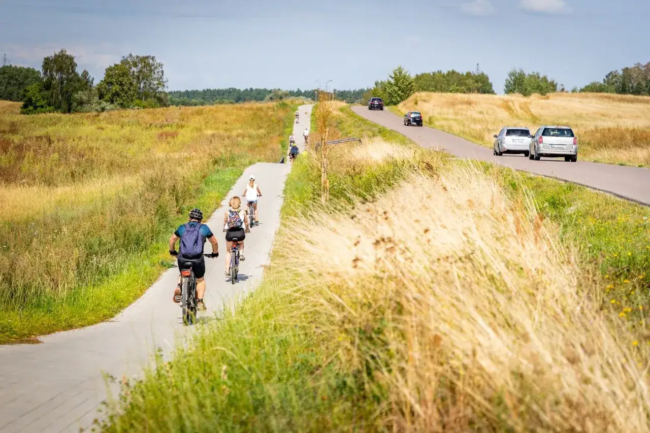 Grupa rowerzystów przemierza malowniczą trasę rowerową na Mazurach, otoczoną polami i drzewami.