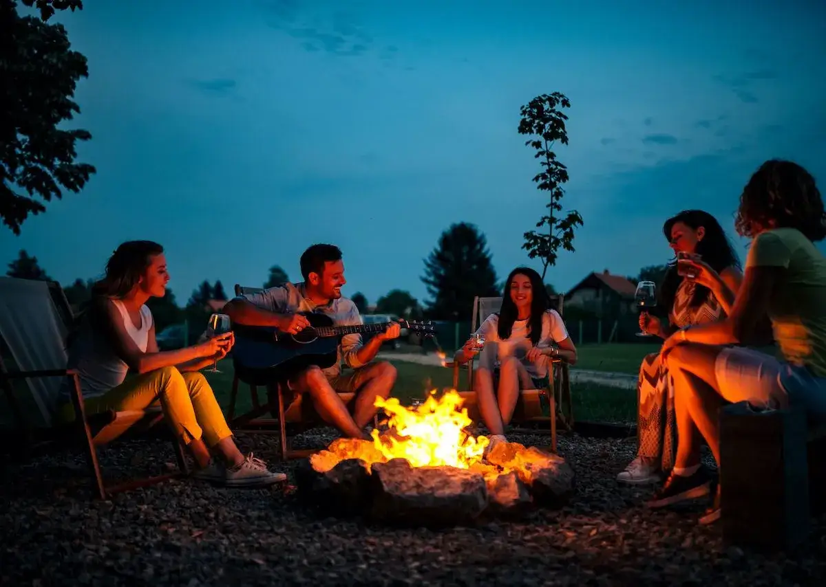 Freunde singen Lagerfeuer Lieder zum Mitsingen, w&auml;hrend einer am Lagerfeuer Gitarre spielt.