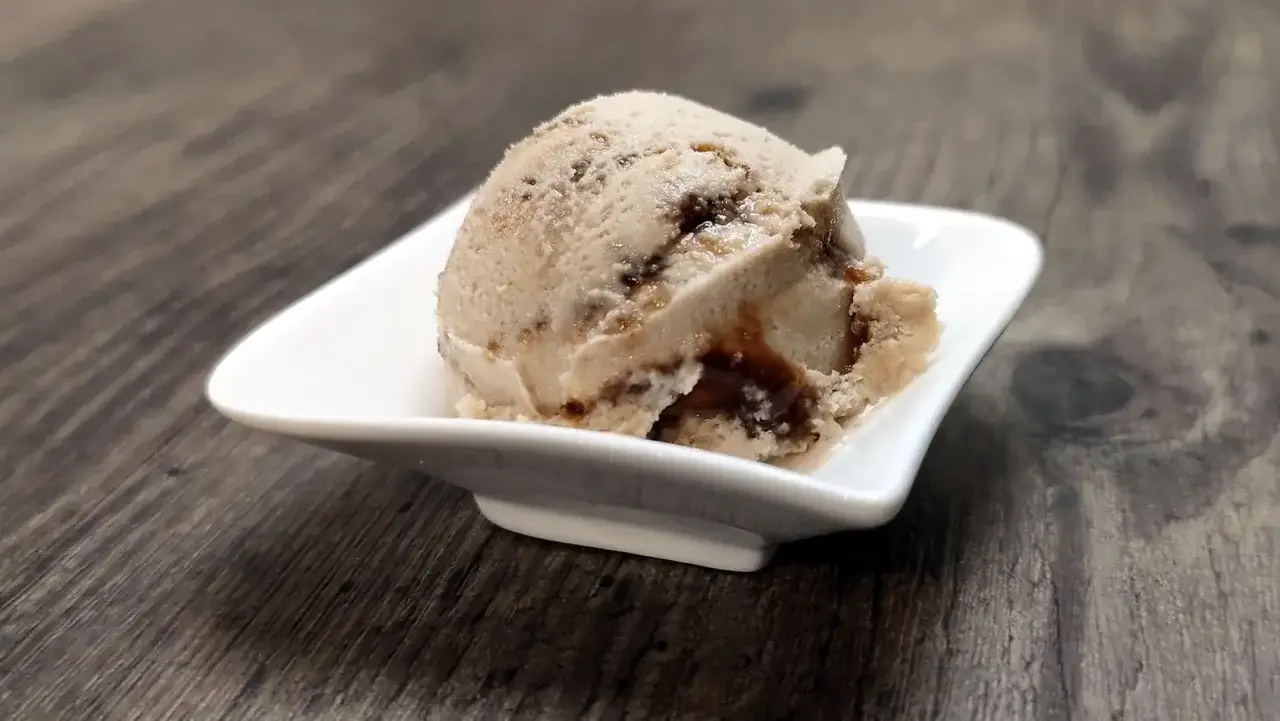 Ein Löffel hausgemachtes Gelato mit Schokoladenstückchen in einer weißen Schale auf Holzhintergrund.