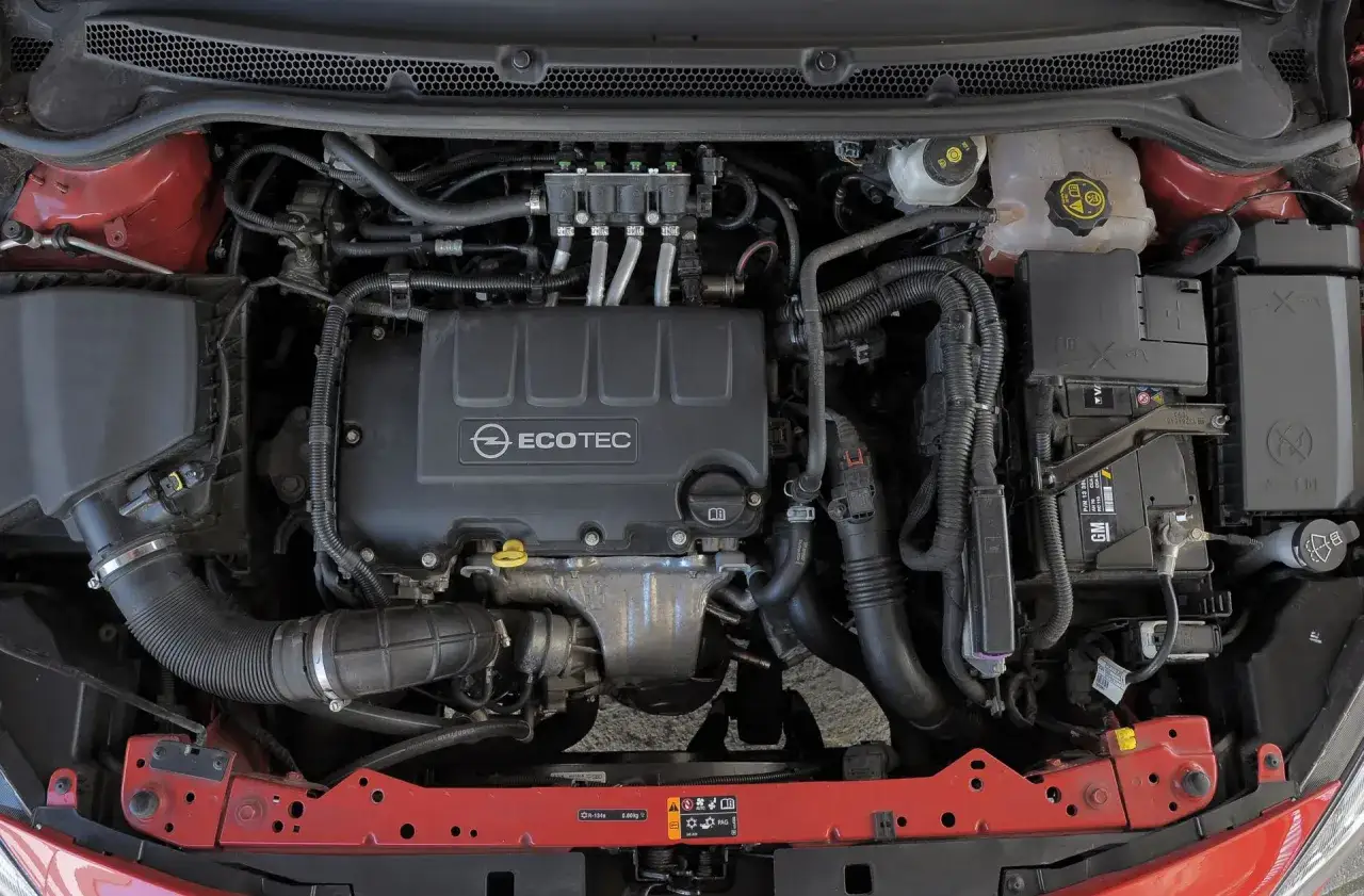 Silnik Opel Astra J 1.6 benzyna, widok z góry. Widać pokrywę silnika Ecotec, przewody, akumulator GM i elementy układu chłodzenia.