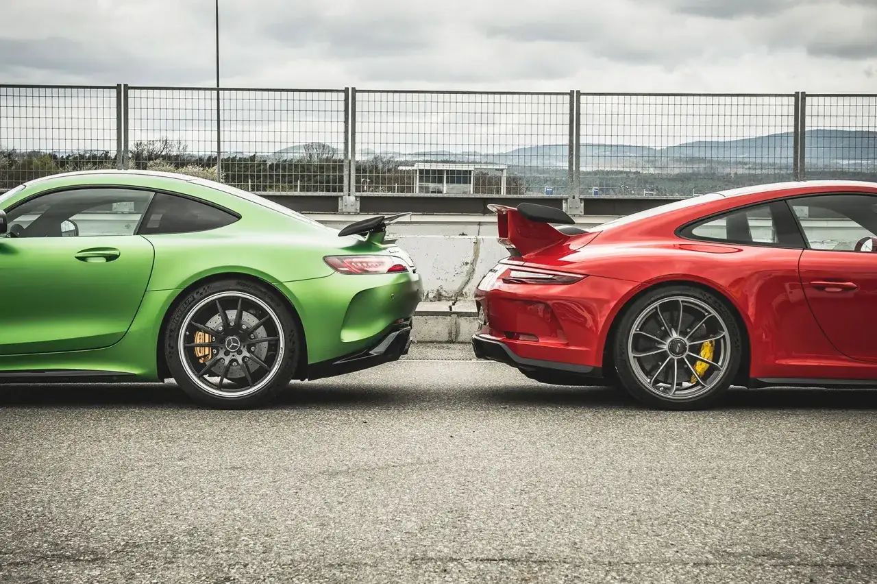 Zielony Mercedes-AMG GTR Pro i czerwony samochód sportowy stoją obok siebie na torze wyścigowym.