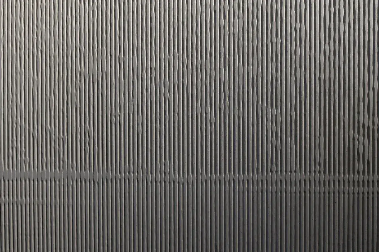 Strukturierte Betonwand mit vertikalen Rillen, die an eine Wellenform erinnern. Ideal, wenn Sie Sichtbeton selber machen möchten und eine einzigartige Textur suchen.