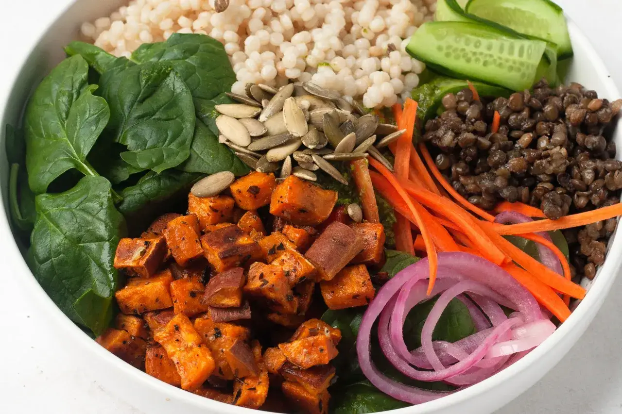 Un bol coloré avec des dés de patate douce rôtie, des lentilles, des épinards, des carottes râpées, des concombres et des graines. Parfait pour une recette de freekeh.
