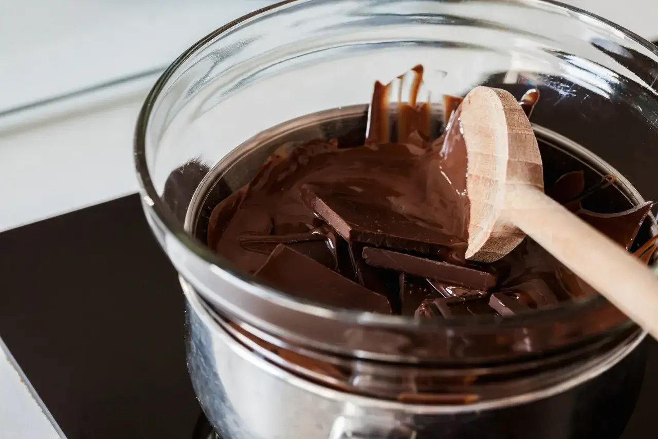 Chocolat noir en morceaux fond dans un bain-marie, une cuillère en bois est prête à remuer. Le chocolat durci attend d'être transformé.