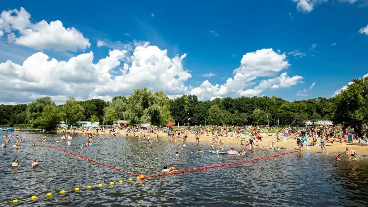 Tłum ludzi odpoczywa na plaży i kąpie się w jeziorze w Poznaniu. Słoneczny dzień, błękitne niebo z białymi chmurami.