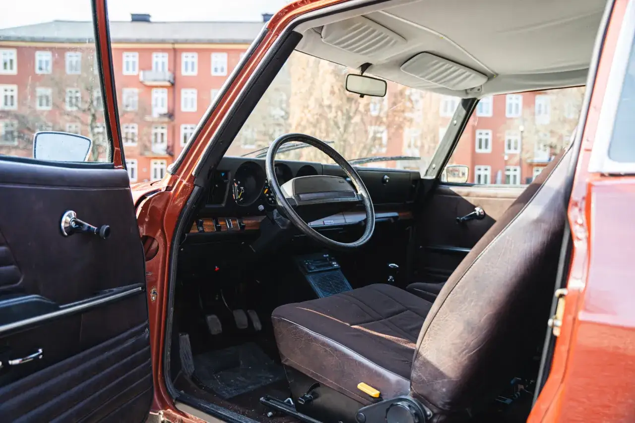 Interiör i en klassisk orange Saab 99. Mörka tygsäten och instrumentpanel med trädetaljer.