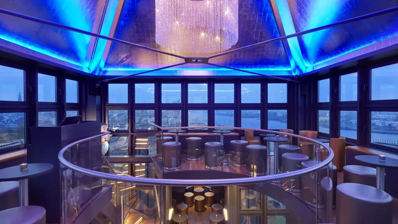 Modernes Restaurant mit atemberaubender Aussicht auf den Hamburg Hafen. Blaue Beleuchtung und ein Kronleuchter schaffen eine luxuri&ouml;se Atmosph&auml;re.