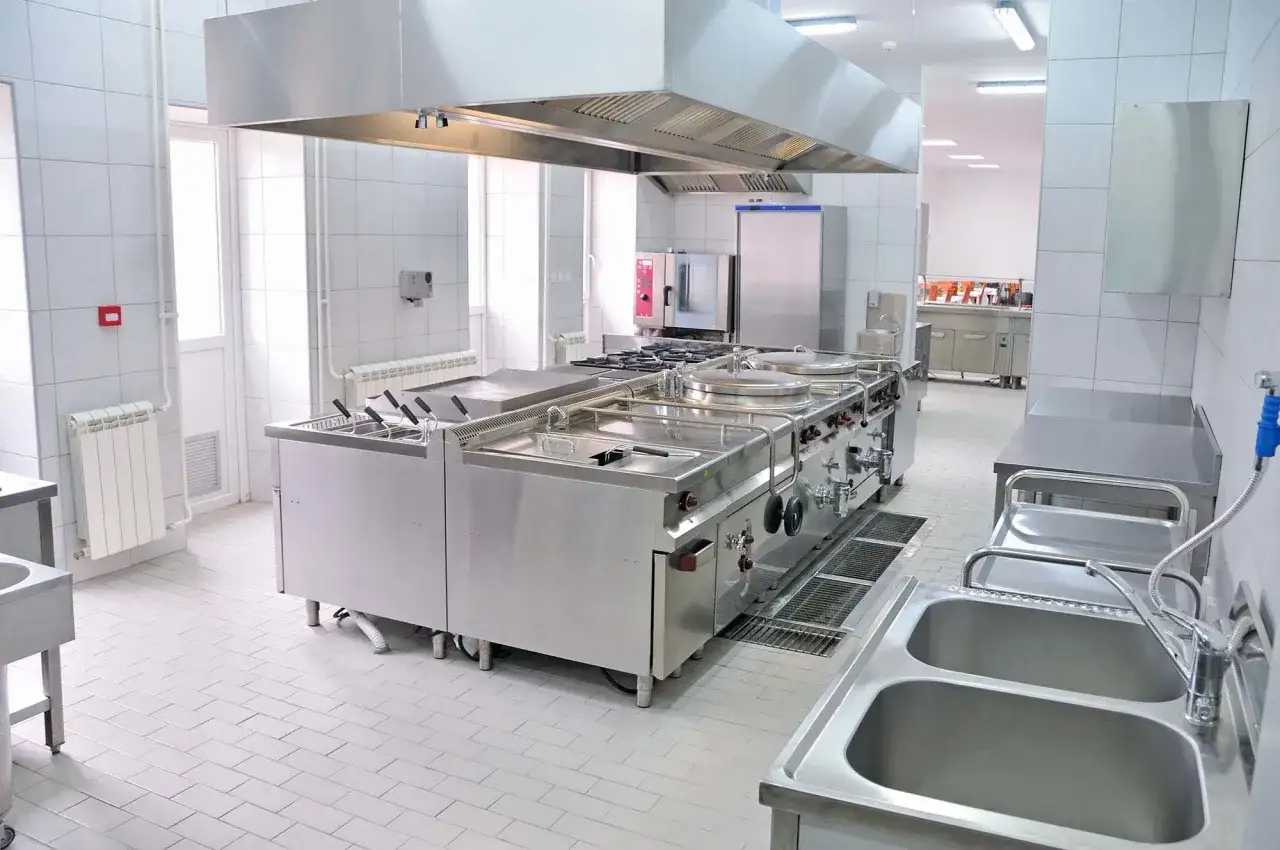 Cocina industrial de acero inoxidable, con fogones, hornos y fregaderos. Este tipo de cocina está diseñada para la preparación de grandes volúmenes de comida.