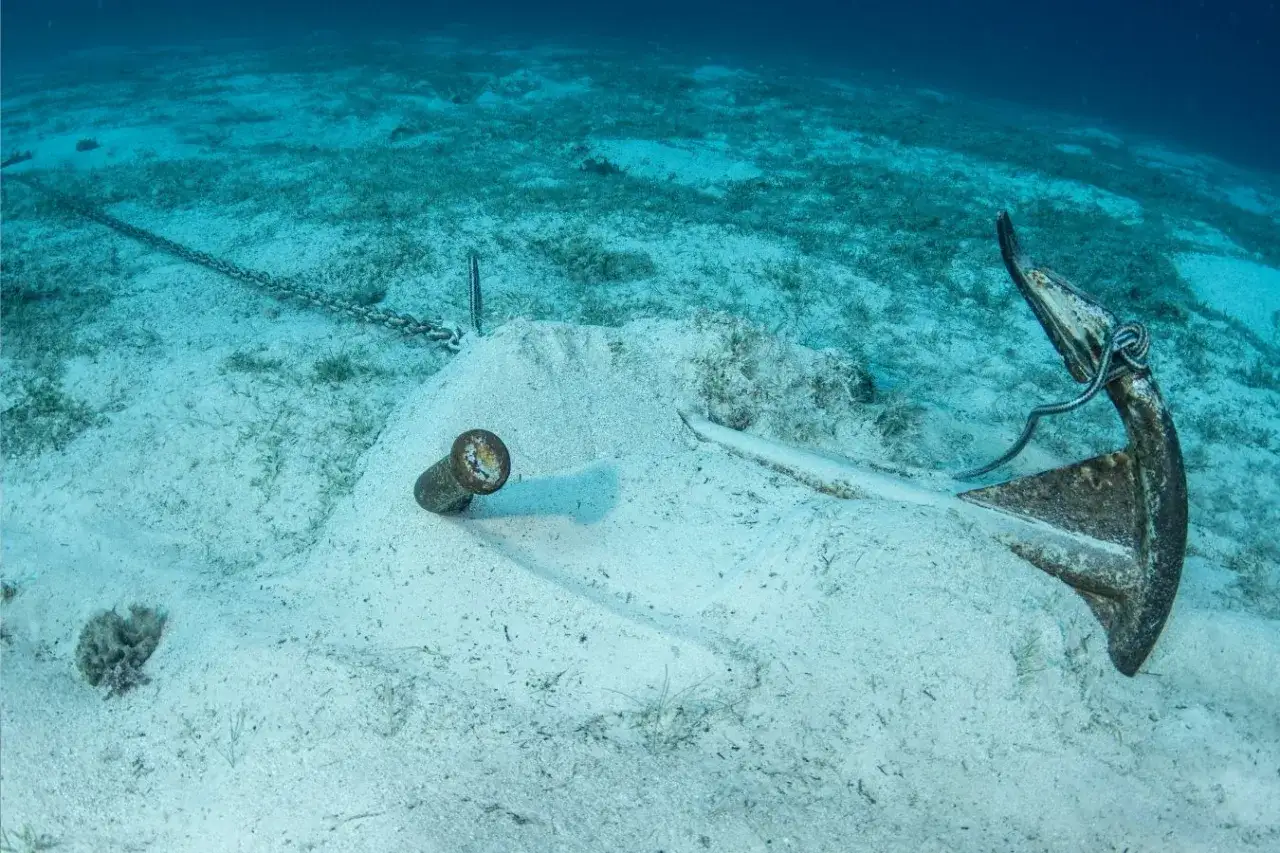 Ancre de bateau rouillée sur fond sableux, chaîne s'étendant vers la gauche. Une vision sous-marine qui rappelle comment remonter une ancre de bateau.