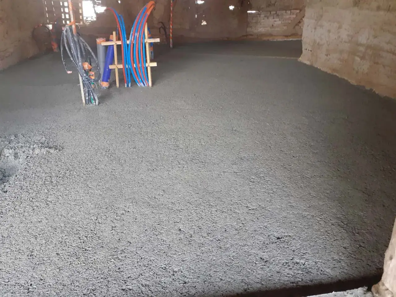 Une nouvelle dalle chaux chanvre en cours de pose, avec des tuyaux de chauffage au sol qui émergent.