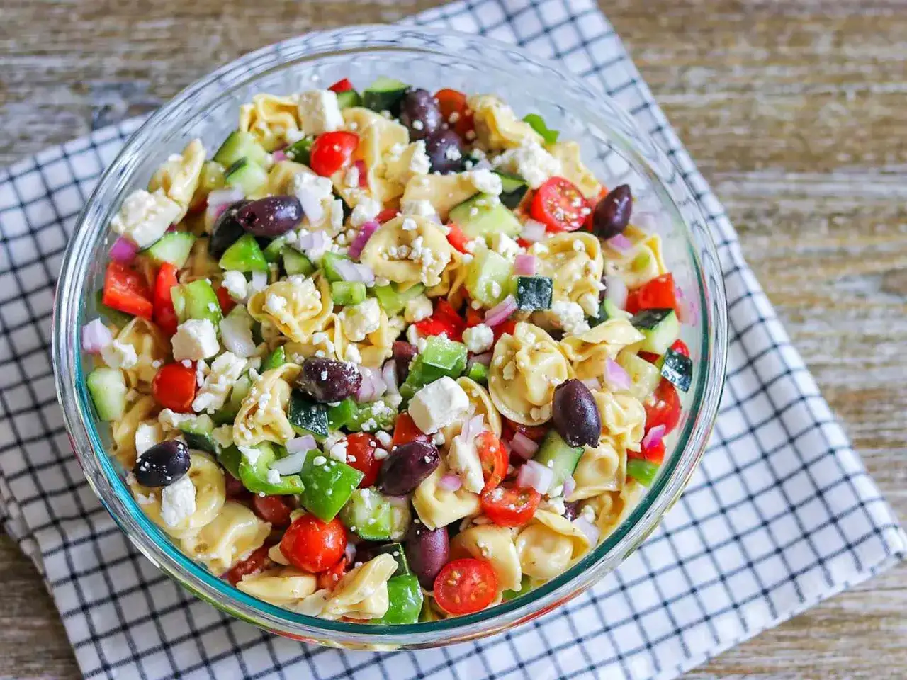 Frischer tortellini salat mediterran mit Tomaten, Gurken, Oliven, Paprika und Feta in einer Glasschüssel.