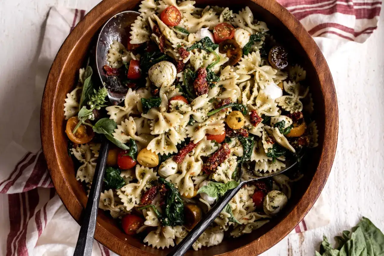 En stor träskål fylld med en härlig pastasallad med fjärilspasta, körsbärstomater, soltorkade tomater, mozzarella och färsk basilika, allt blandat med en smakrik pesto.
