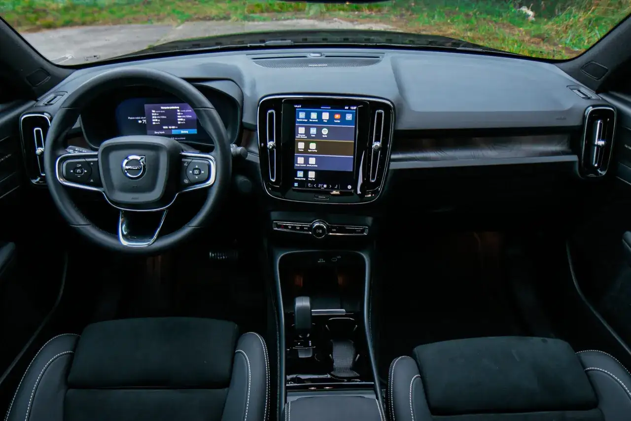 Wnętrze Volvo C40: kierownica, cyfrowy kokpit i ekran multimedialny z aplikacjami. Widoczne czarne fotele z białymi przeszyciami.