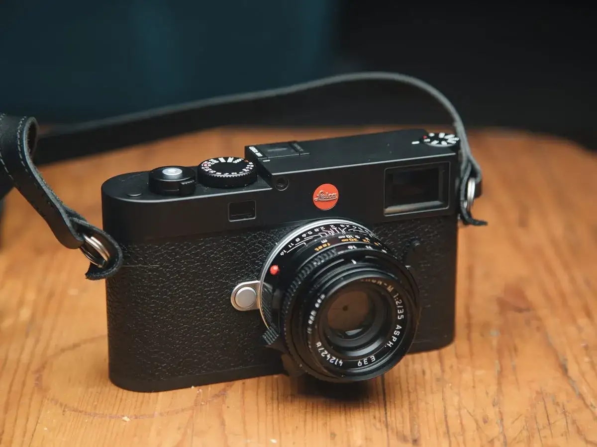 A black Leica M11 camera with a leather strap rests on a wooden surface, ready for its next photographic adventure.
