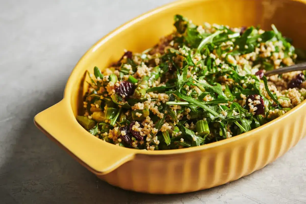 Insalata di miglio colorata con asparagi, rucola e mirtilli rossi in una ciotola gialla.