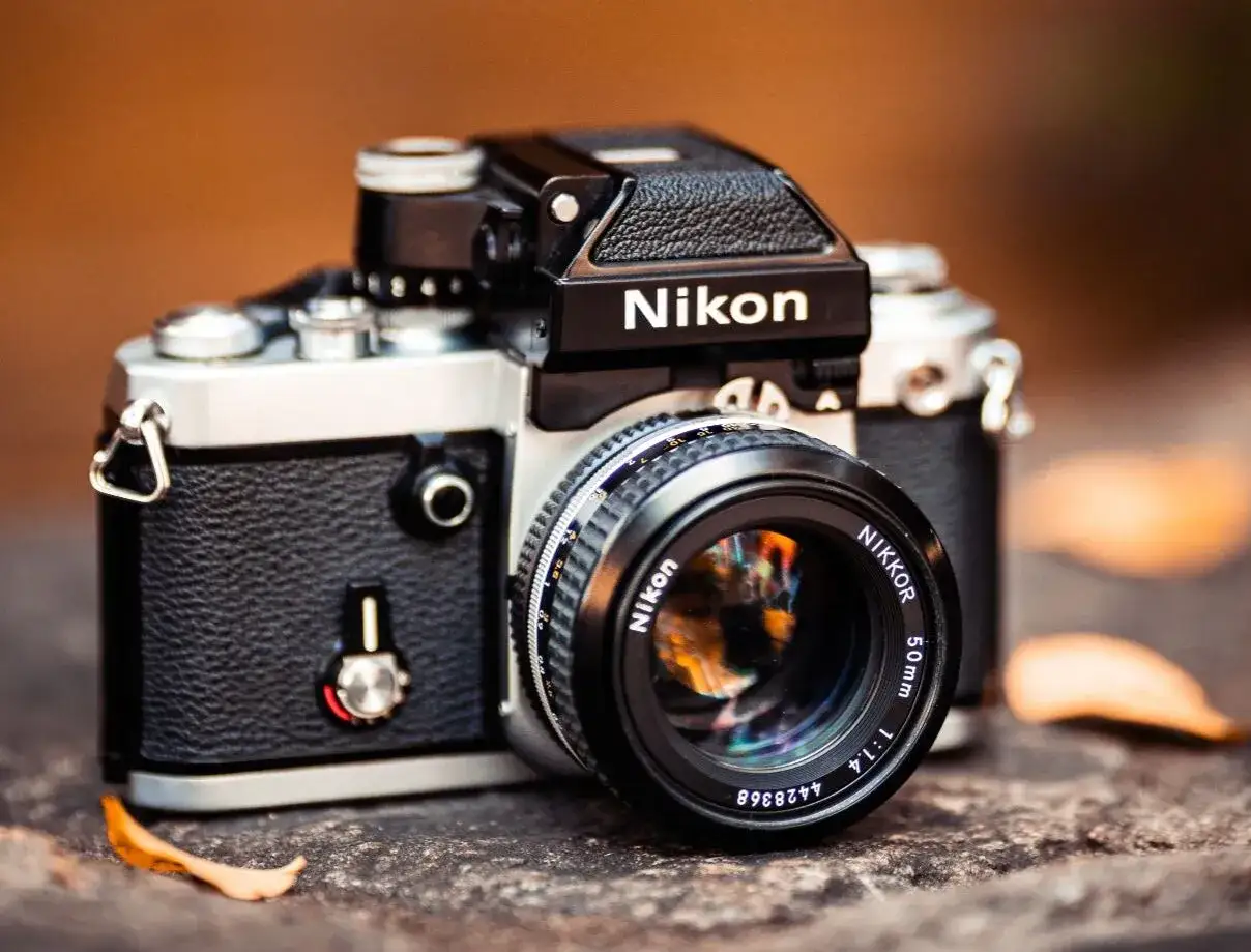 A classic Nikon film camera, a testament to highest quality film camera craftsmanship, rests on a textured surface with fallen leaves.