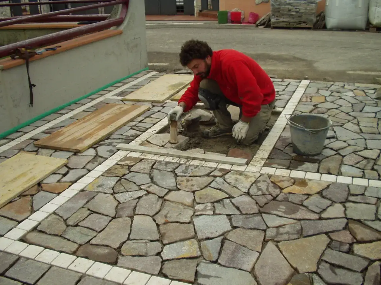 Operaio posa pietre irregolari su un marciapiede in pietra, creando un disegno unico.