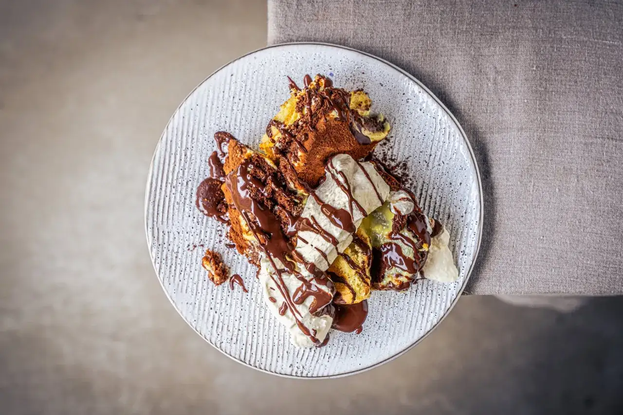 Ein köstlicher Somlauer Nockerl-Dessert mit Schokoladensauce und Eiscreme, bestäubt mit Kakaopulver.