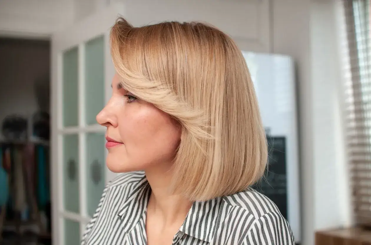 Kobieta z blond bobem z grzywką, w koszuli w paski, patrzy w bok.