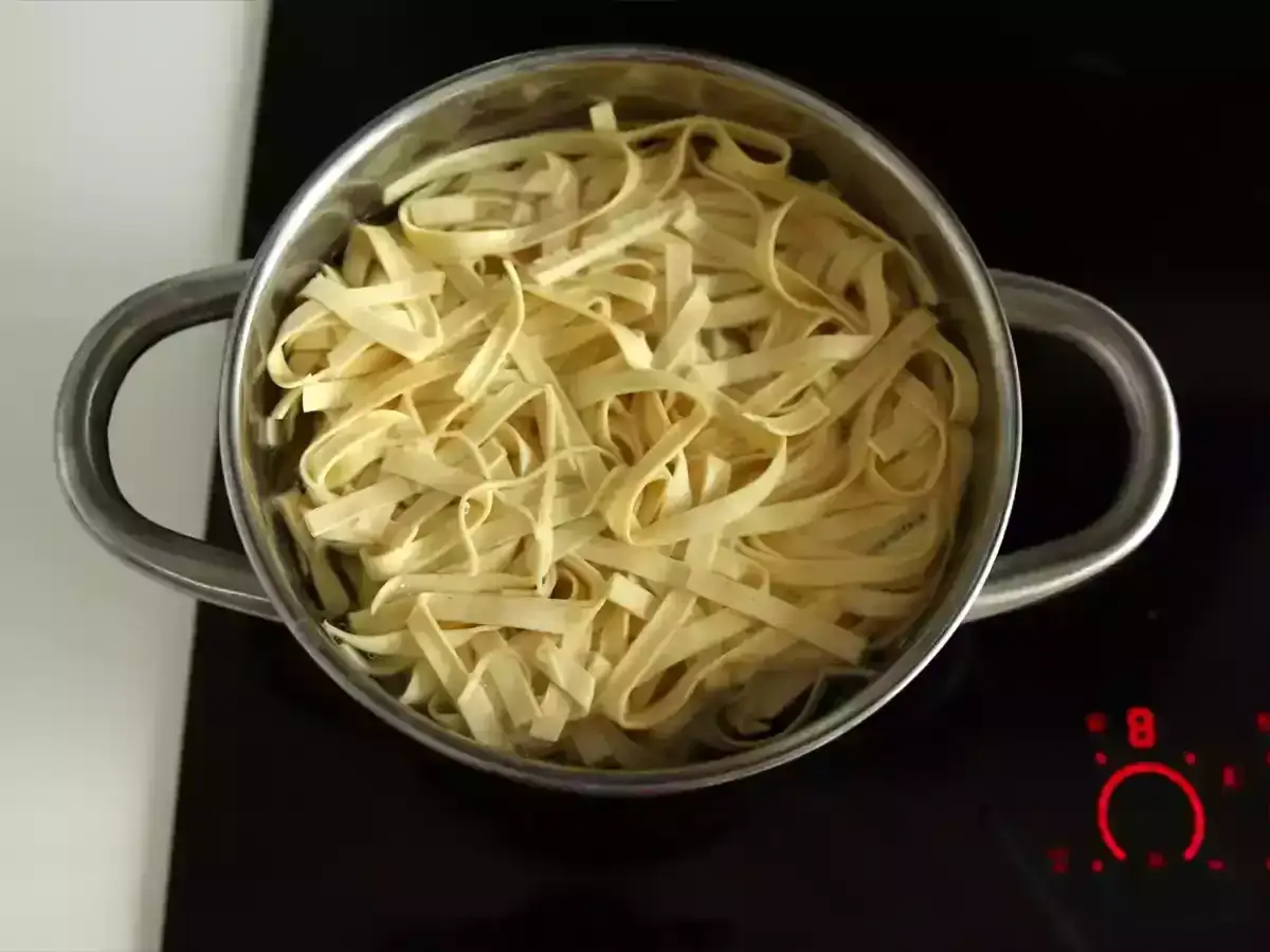Świeży makaron z lodówki w garnku na płycie indukcyjnej. Kontrastuje z suchym makaronem z paczki, który czeka na swoją kolej.