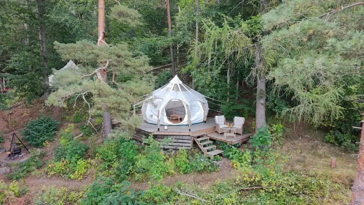 En vit glampingtält på en träaltan i skogen, en del av nyrups naturhotell. Utanför tältet finns en sittgrupp.