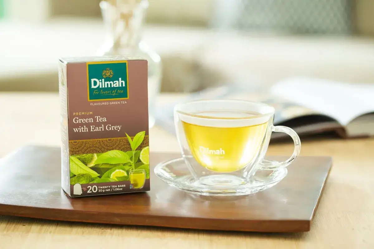 Pudełko herbaty Dilmah Green Tea with Earl Grey obok filiżanki z naparem. Idealny wybór dla miłośników herbaty.