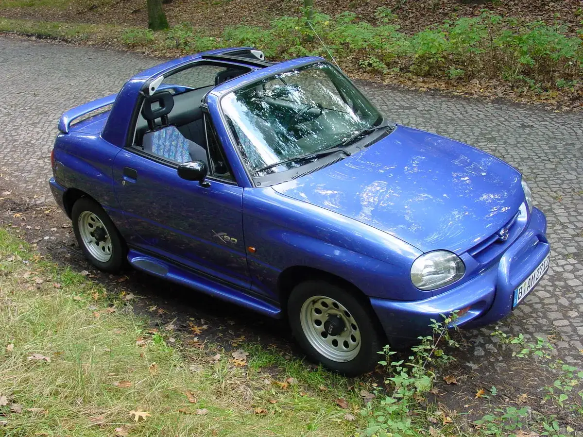Niebieski Suzuki X90 z otwartym dachem stoi na kamienistej drodze, otoczony zielenią.