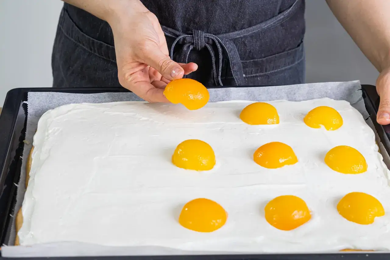 Ein einfacher spiegeleierkuchen wird mit Pfirsichh&auml;lften belegt. Die s&uuml;&szlig;en Fr&uuml;chte liegen auf einer cremigen wei&szlig;en Schicht.