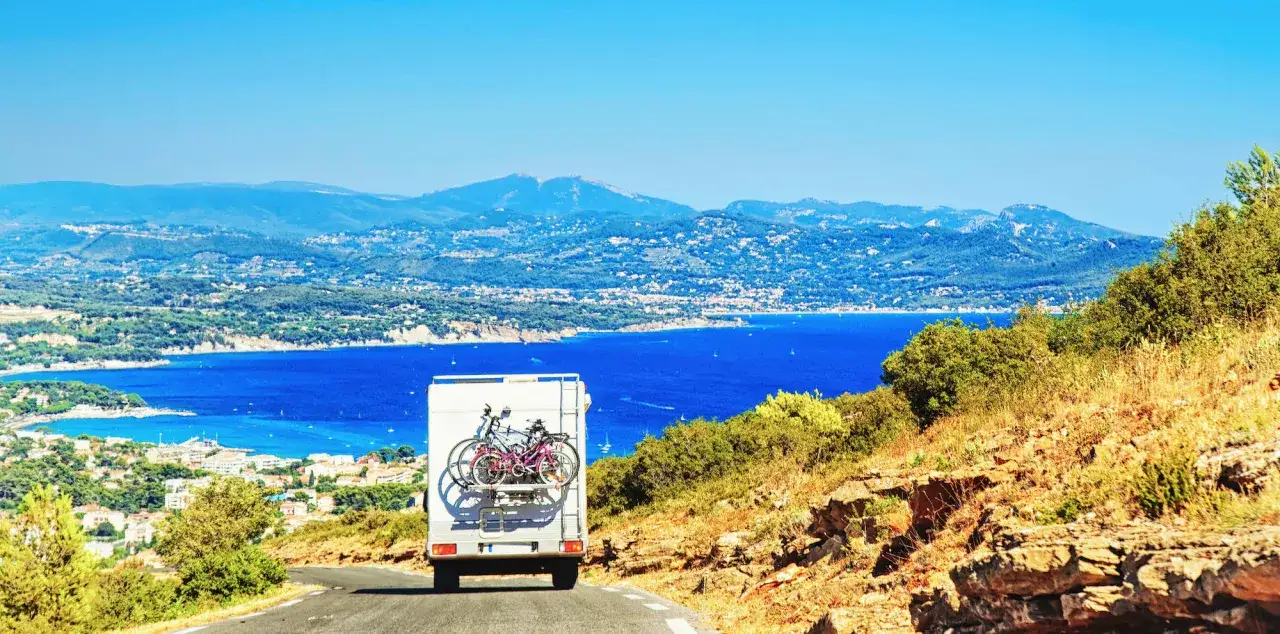 Camping-car avec vélos, explorant les paysages côtiers de l'Italie du Nord. La mer d'un bleu profond contraste avec les montagnes verdoyantes.