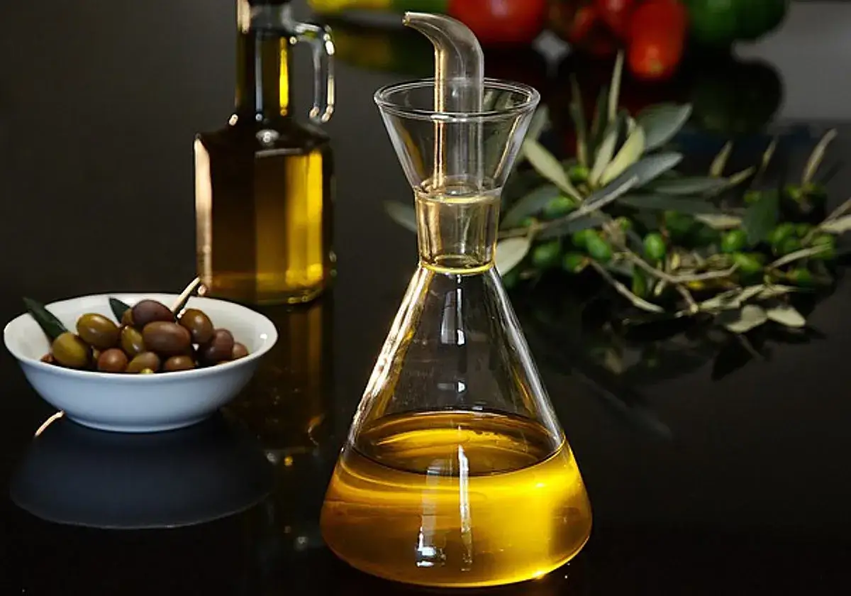 Aceite de oliva en un decantador, junto a un cuenco de aceitunas y una rama de olivo. Ideal para tus recetas con aceite de oliva.