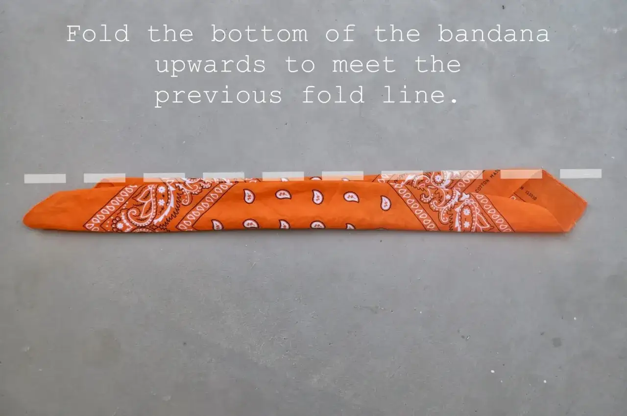 Orange bandana vikt på mitten. Lär dig hur knyter man en bandana för en snygg stil.