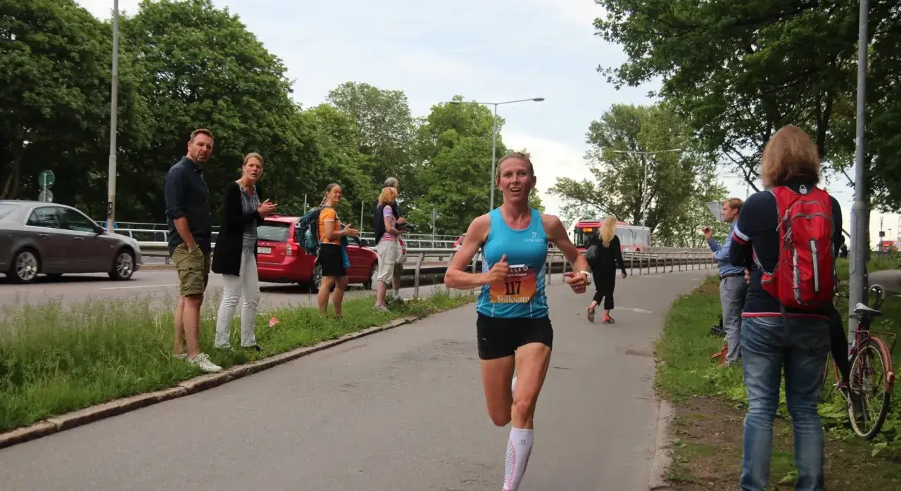 En kvinna springer i ett adidas halvmarathon, med publik som hejar l&auml;ngs banan.