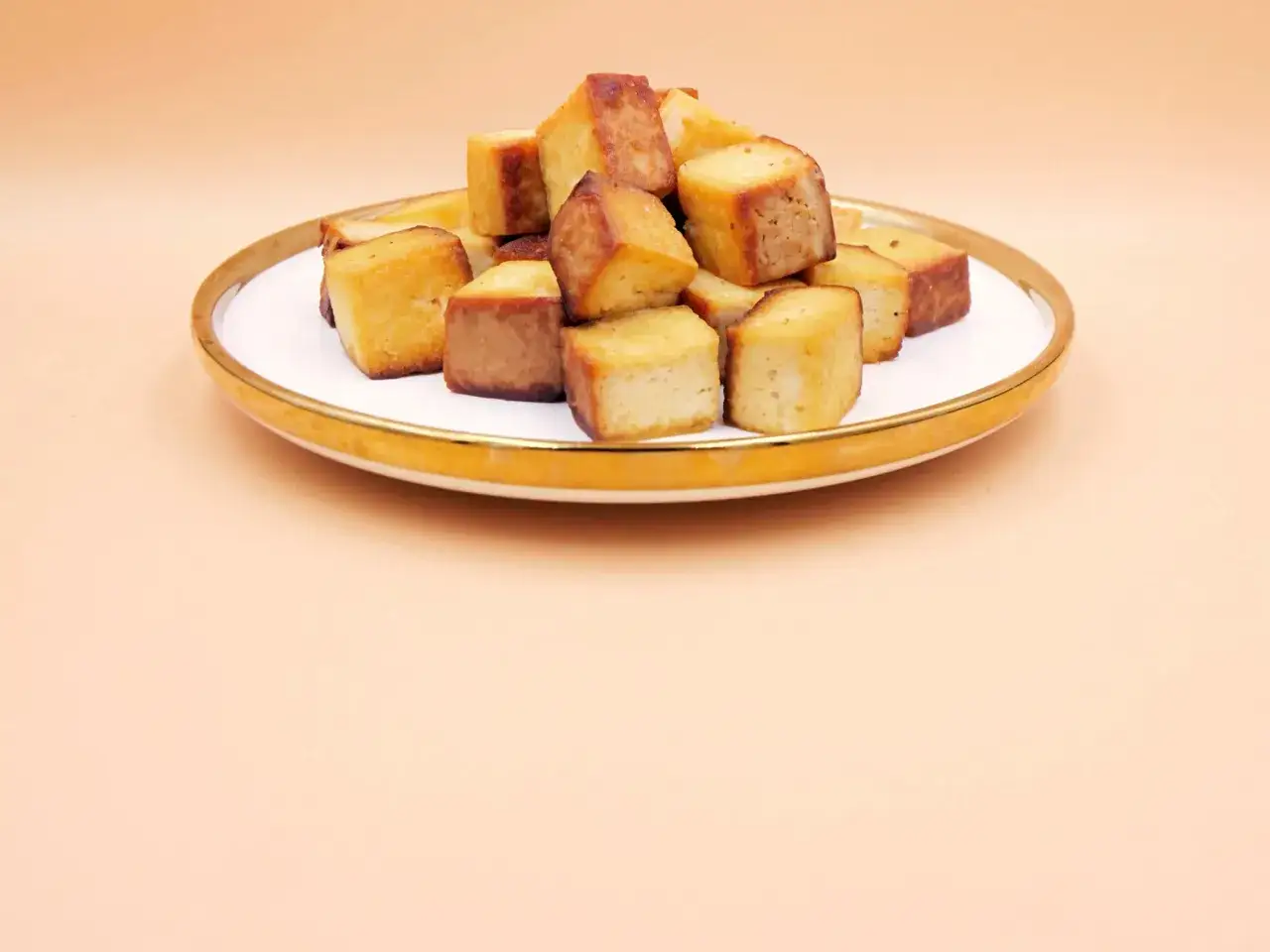 Złociste kostki tofu na talerzu, gotowe do dalszego wykorzystania. Prosty sposób, jak przyrządzić tofu na chrupko.