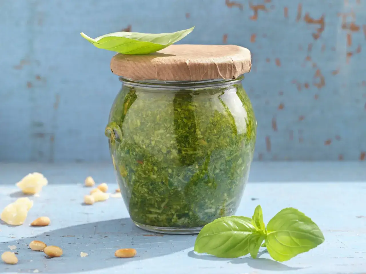 Frisches Basilikumpesto im Glas, umgeben von Pinienkernen und Parmesan. Perfekt für leckere Pesto Rezepte.