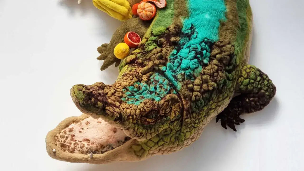 Un crocodile en feutre, &oelig;uvre d'un artiste textile, orn&eacute; de fruits color&eacute;s. Ses &eacute;cailles textur&eacute;es et ses touches de turquoise &eacute;voquent une cr&eacute;ature fantastique.