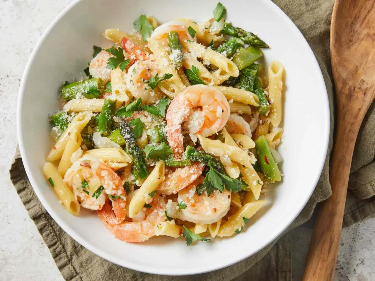 Penne z krewetkami, szparagami i parmezanem, posypane świeżą pietruszką. Pyszne danie, które zachwyci każdego miłośnika makaronu z krewetkami.