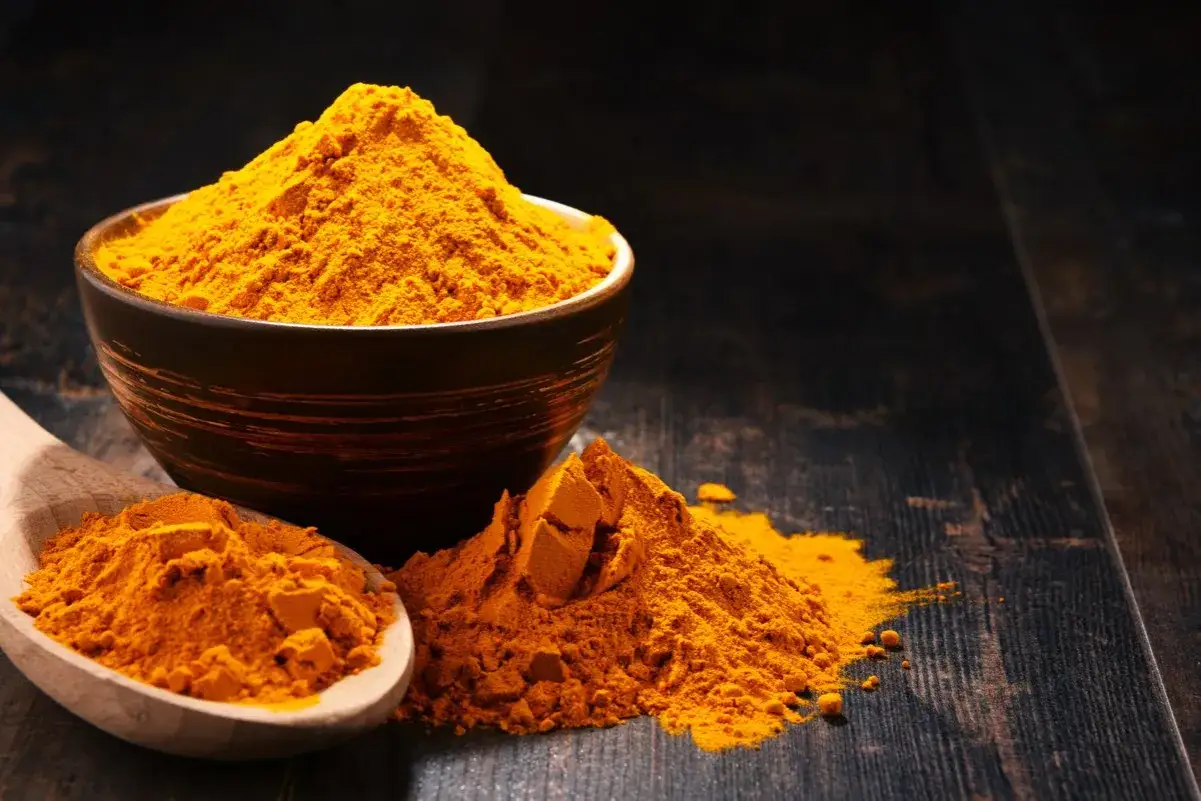 Polvo de raíz de cúrcuma en un cuenco y cuchara de madera, listo para añadir color y sabor a tus platos.