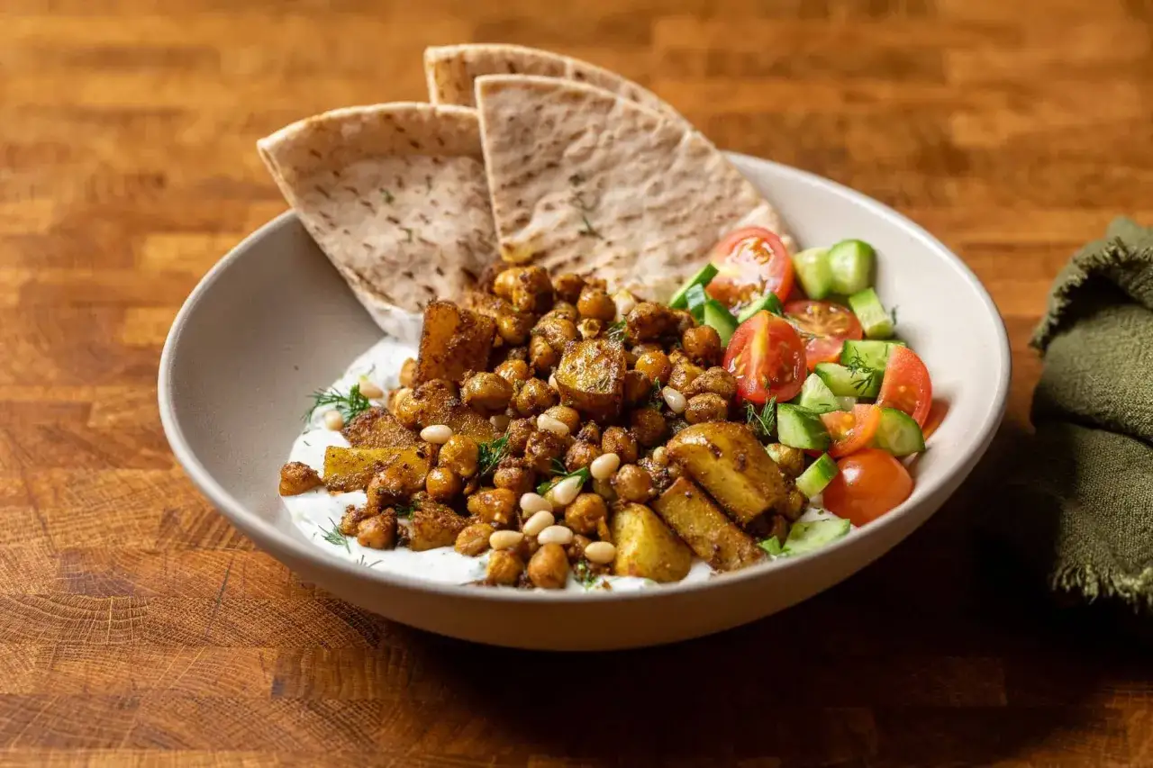 Un bol app&eacute;tissant avec une recette v&eacute;g&eacute;tarienne : pois chiches &eacute;pic&eacute;s, pommes de terre r&ocirc;ties, sauce blanche cr&eacute;meuse, salade fra&icirc;che et pain pita.