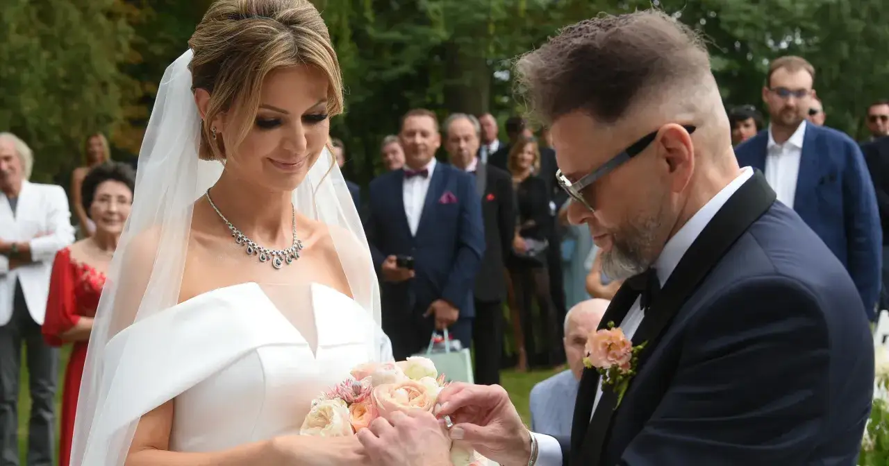 Robert Rutkowski z żoną Joanną podczas ceremonii ślubnej. Pan młody zakłada obrączkę na palec panny młodej.