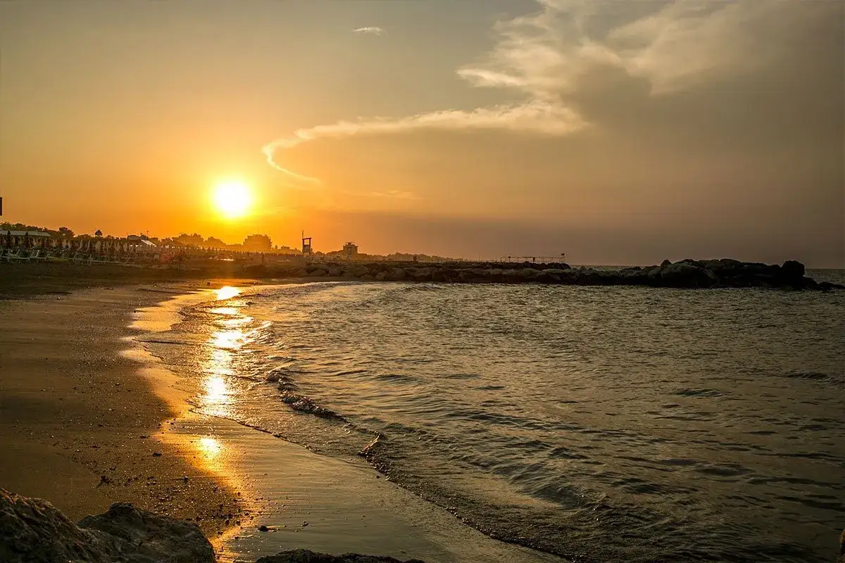 Tramonto dorato su una spiaggia di Misano Adriatico. Le onde lambiscono la riva, mentre il sole illumina la costa. Cosa vedere? La bellezza di questo momento.