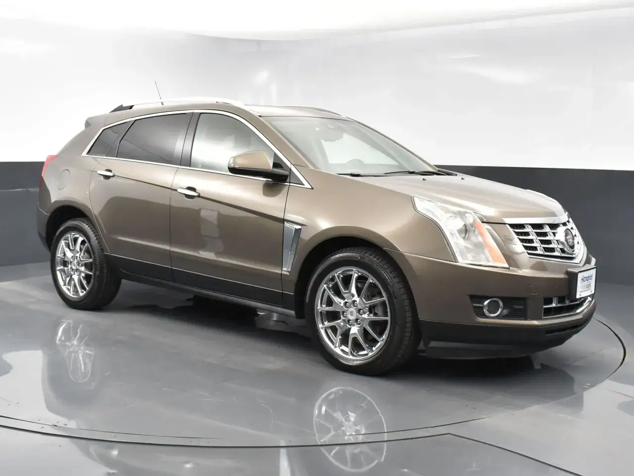 Brązowy Cadillac SRX z chromowanymi felgami stoi na obrotowej platformie.
