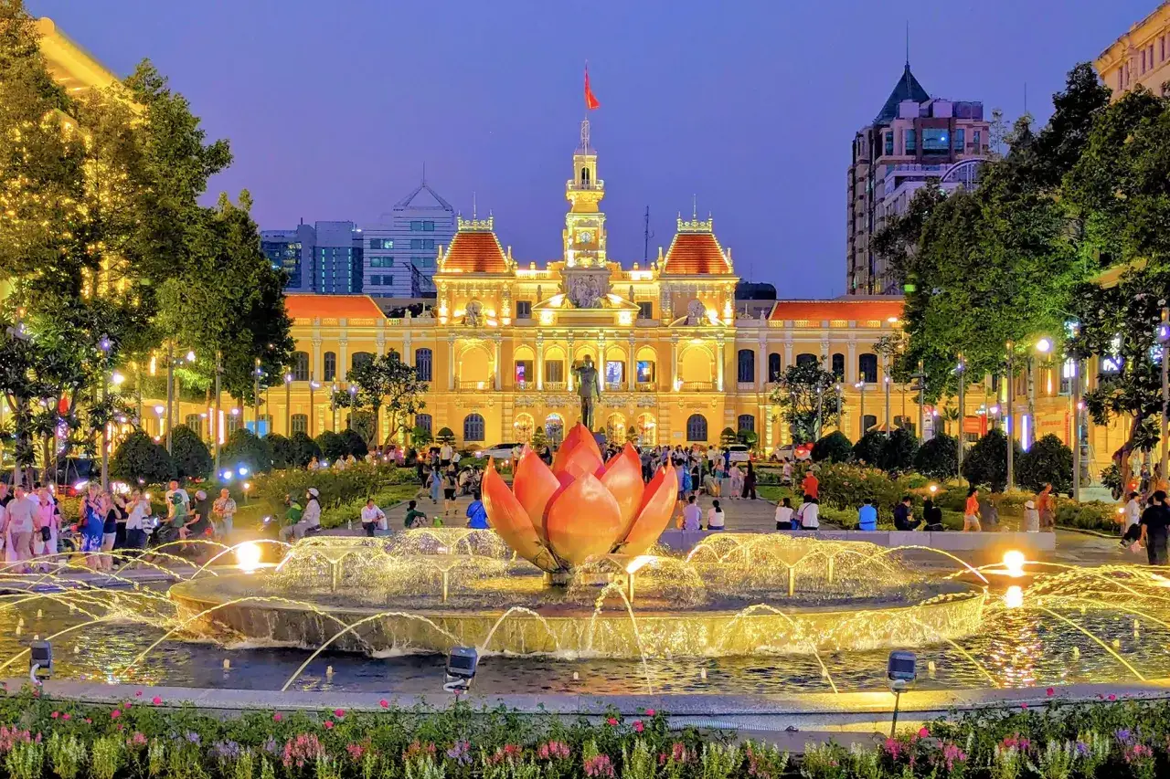 Wieczorny plac w Ho Chi Minh Miasto. Podświetlona fontanna z kwiatem lotosu i ratusz w tle.