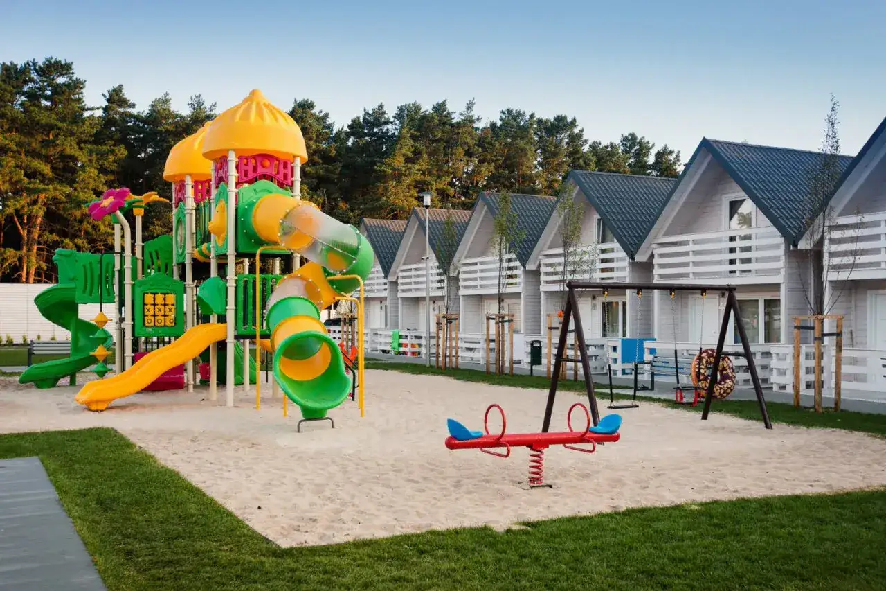 Kolorowy plac zabaw z domkami w tle. Idealne miejsce na rodzinne wakacje, o czym świadczą pozytywne holiday park & resort Grzybowo opinie.