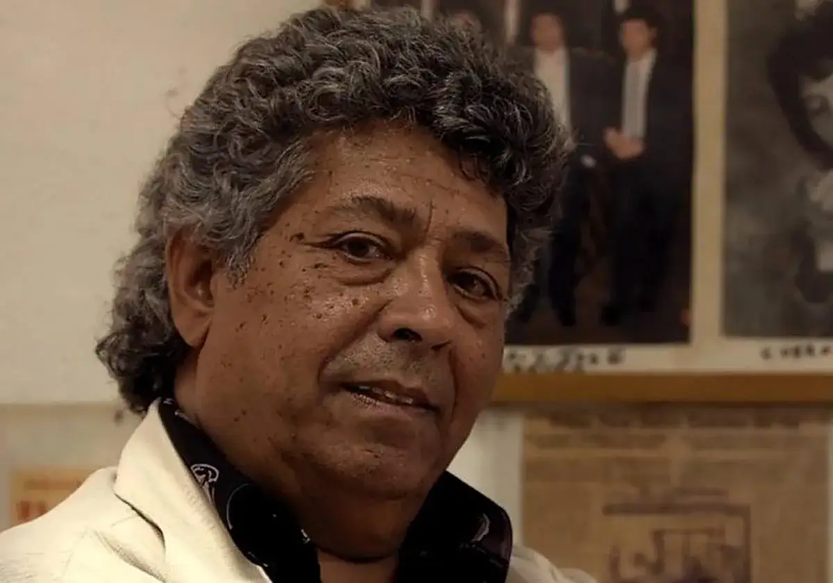 Primer plano de un cantante sevillano flamenco, con su caracter&iacute;stico pelo rizado y mirada intensa.