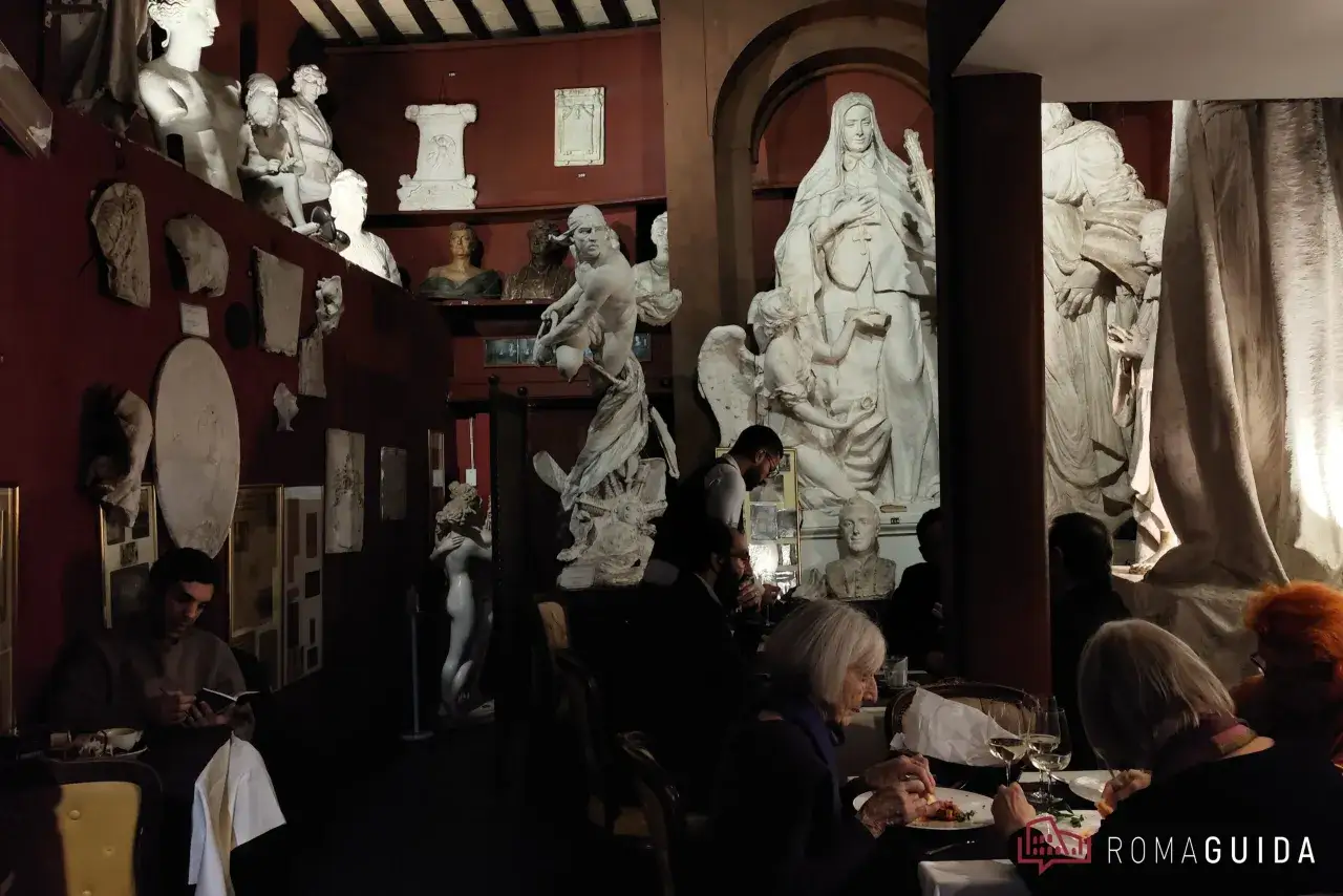 Un caffè a Roma famoso, tra sculture antiche e arte. Persone mangiano e leggono in un ambiente unico.